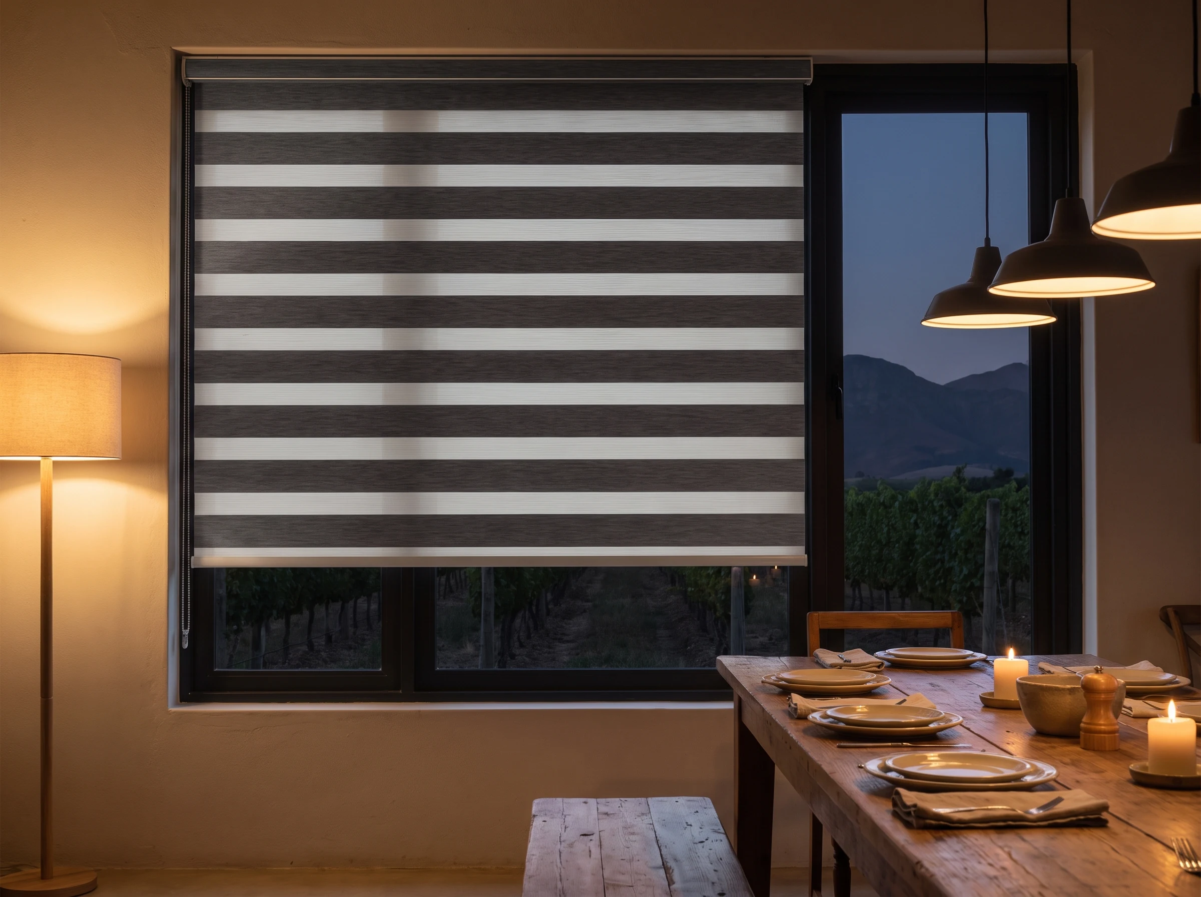 Day and night zebra blind fully closed with bands offset for privacy over a dining room window near Klapmuts at dusk, dinner table set with lamp light